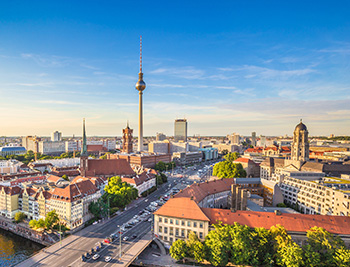 Ansicht der Stadt Berlin aus der Vogelperspektive. Markant ragt der Berliner Fernsehturm in den blauen Himmel.